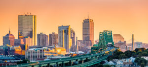 Boston skyline at sunset with elevated train tracks in foreground.