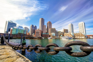 City skyline with waterfront and heavy chains in foreground under blue sky.
