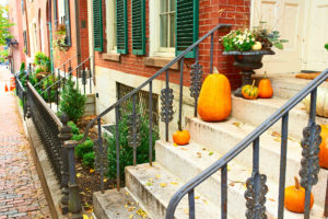 Pumpkins decorate steps of a brick house with green shutters.