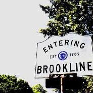 Road sign indicating entry into Brookline with a tree background.